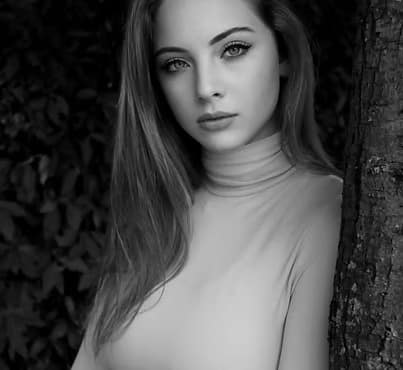 Ritratto in bianco e nero di una giovane donna con capelli lunghi e sguardo intenso, appoggiata a un albero.