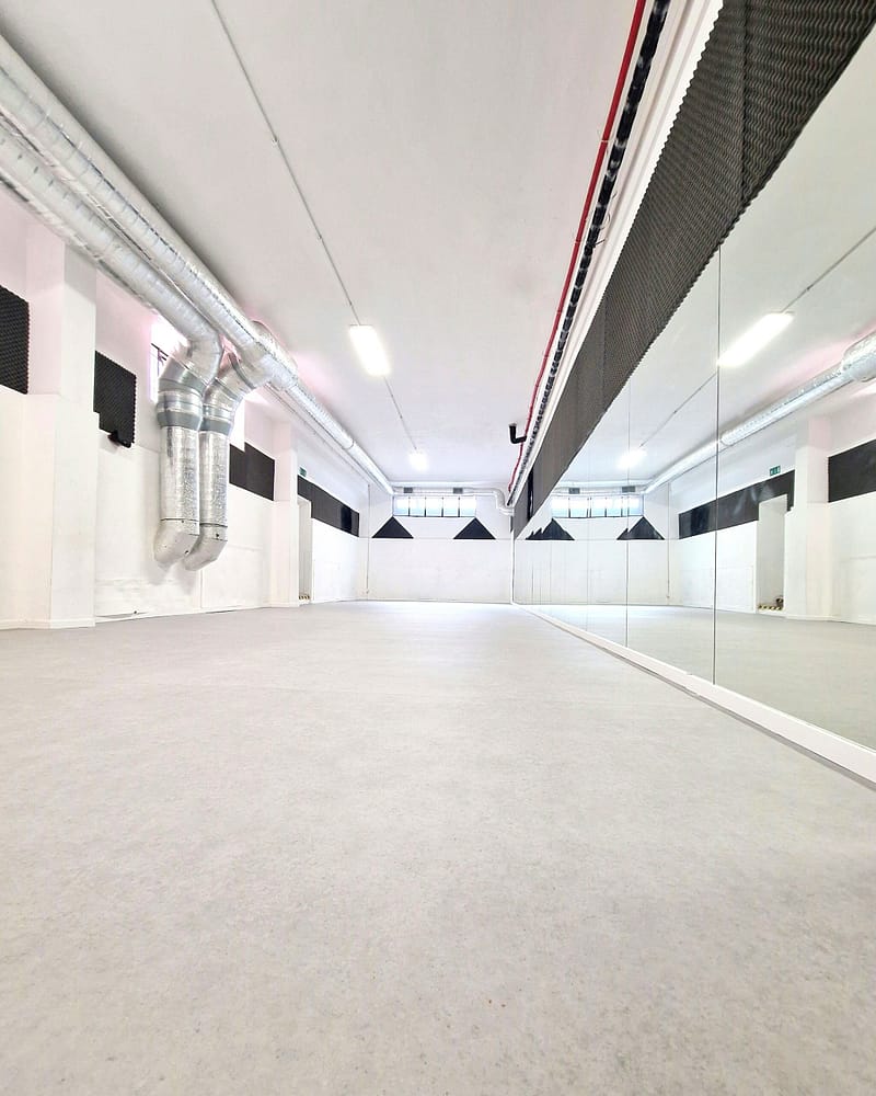 Spazio ampio e vuoto con pareti bianche e specchi, illuminato da luci a soffitto.